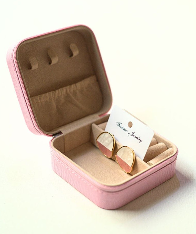 Pink jewelry box with a pair of earrings inside on a light background