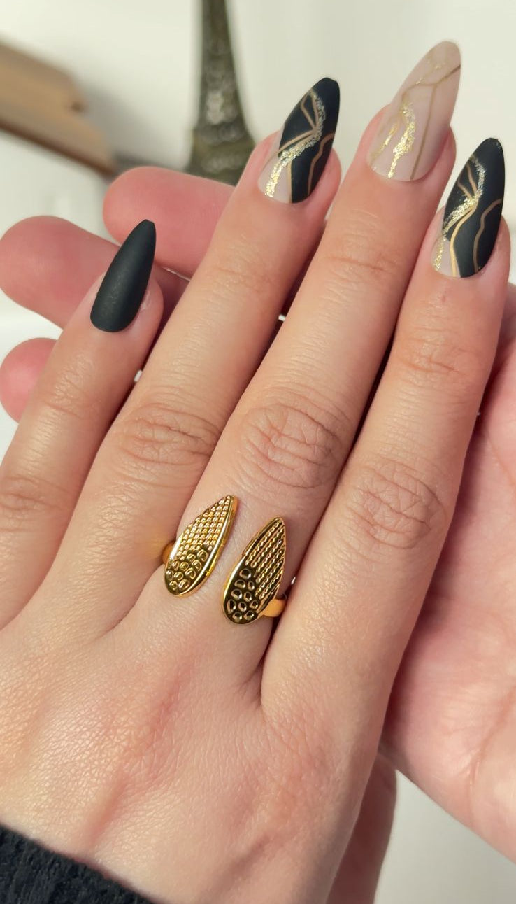 Hand with black, gold, and beige nail designs on a white background