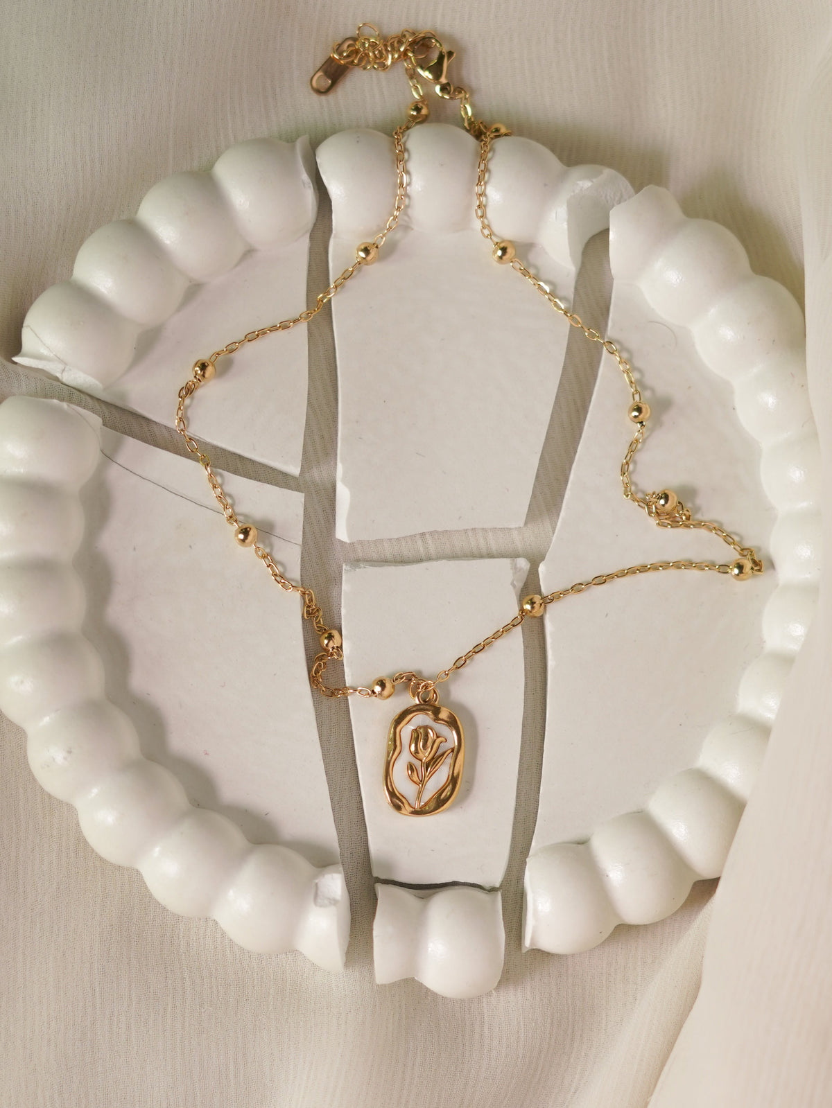 Gold necklace on a white stand with a beige background