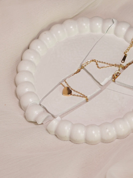 Gold necklace with a heart pendant on a white beaded stand.