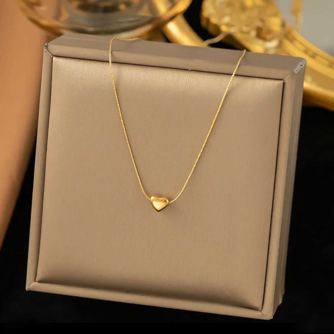 Gold necklace with a heart pendant on a beige jewelry box