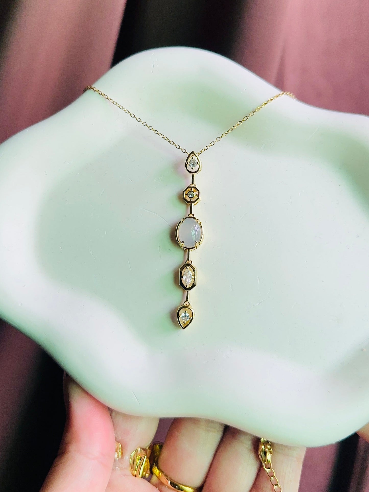 Gold necklace on a white dish held by a hand against a blurred background