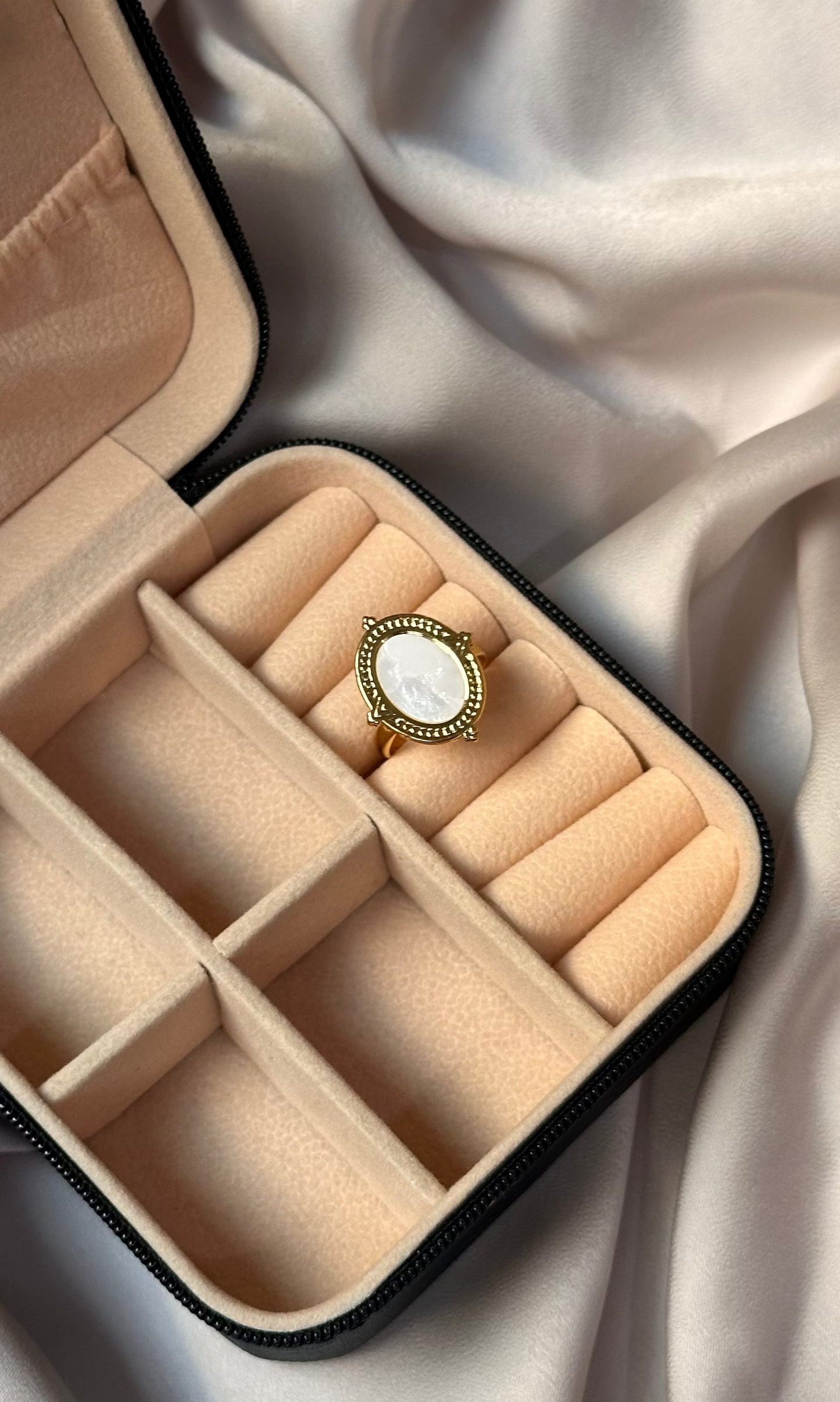 Beige jewelry box with a ring inside on a white fabric background