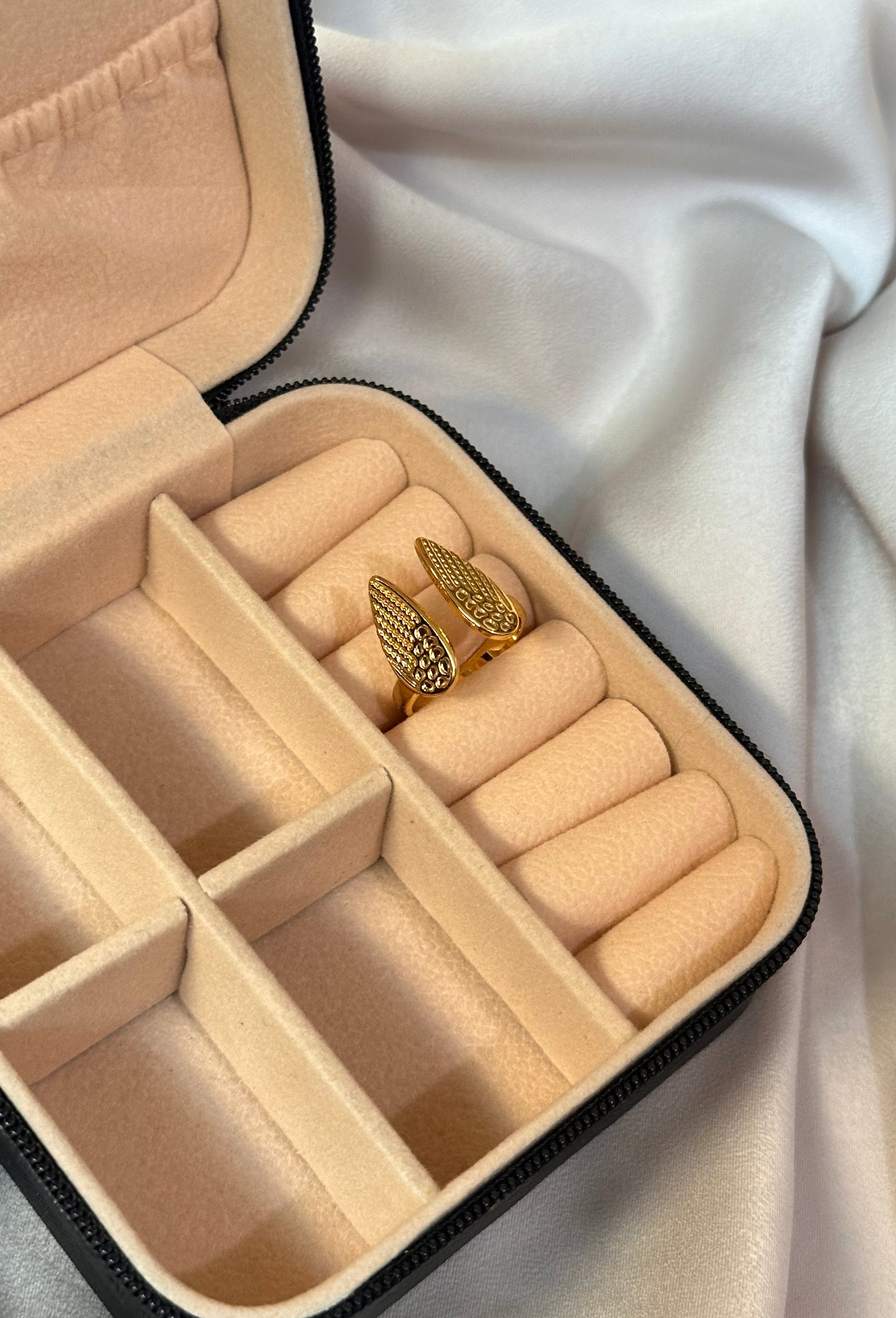 Beige jewelry box with compartments containing gold rings on a white fabric background