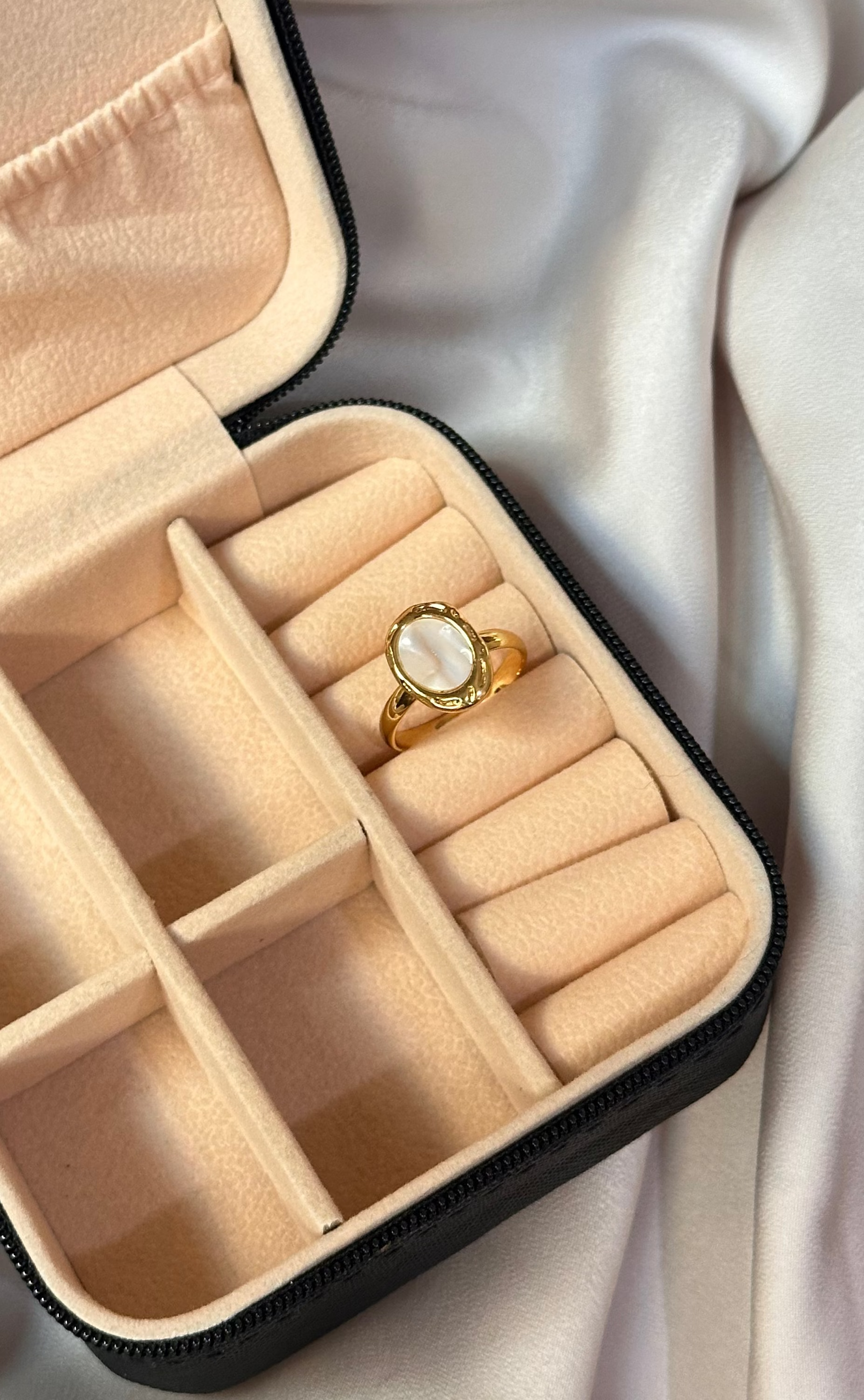 Beige jewelry box with a ring on a light fabric background