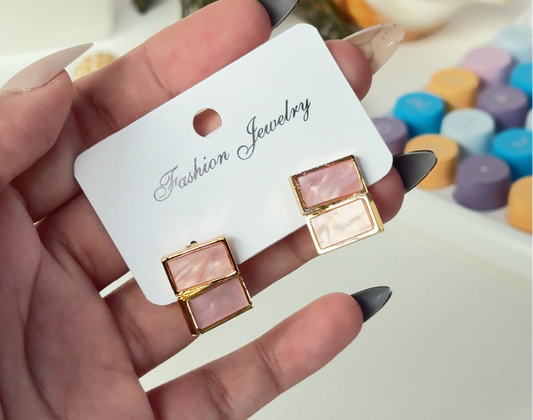 Hand holding a card with earrings in front of a blurred background