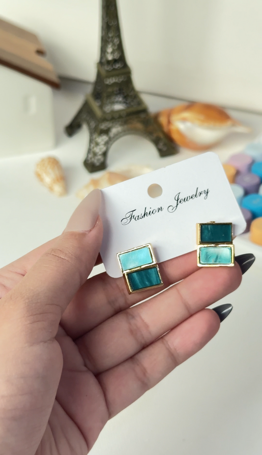 Hand holding a pair of earrings with a blurred background featuring the Eiffel Tower model.