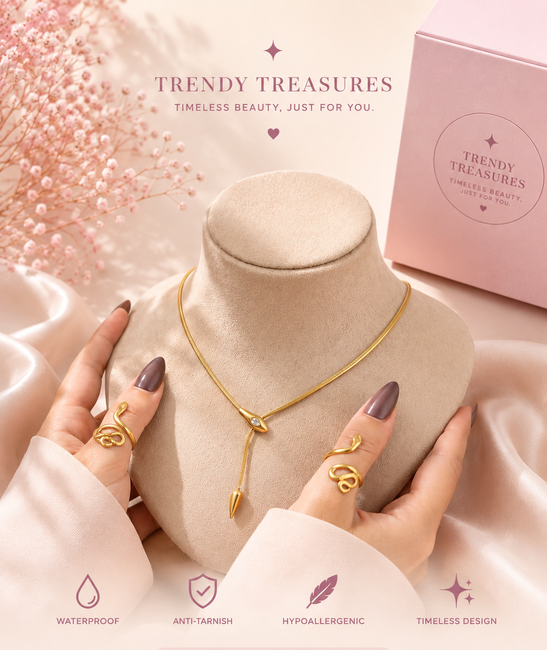 A gold-tone keychain necklace displayed on a beige jewelry bust, held by two hands with mauve manicured nails. The background is a soft pink satin fabric with pink dried flowers, a pink 'Trendy Treasures' box, and promotional text and icons at the bottom.