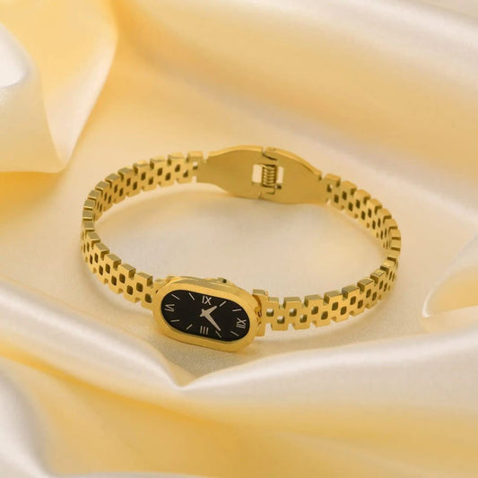 Gold bracelet with a black watch face on a yellow fabric background