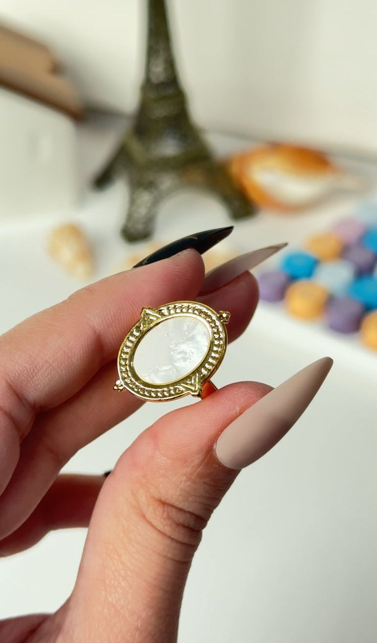 Hand holding a gold ring with a clear stone against a blurred background